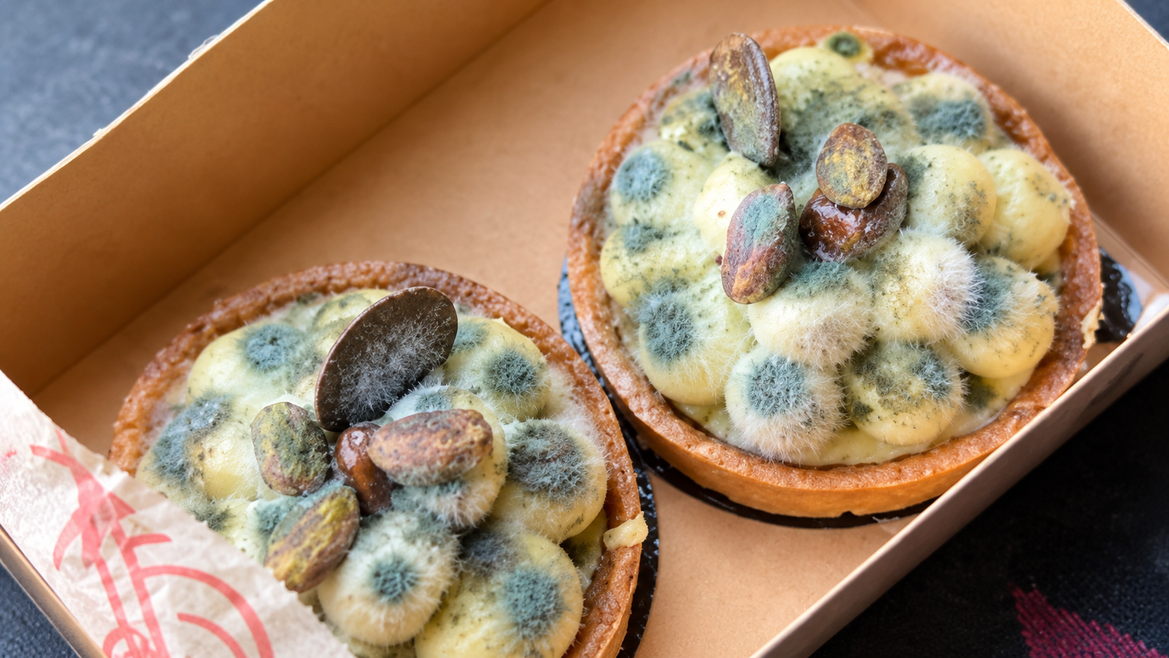 Deux pâtisseries couvertes de moisissure verte et bleue dans une boîte, illustration d’une fraude au remboursement dans laquelle de faux défauts peuvent être ajoutés à une photo grâce à l’intelligence artificielle.