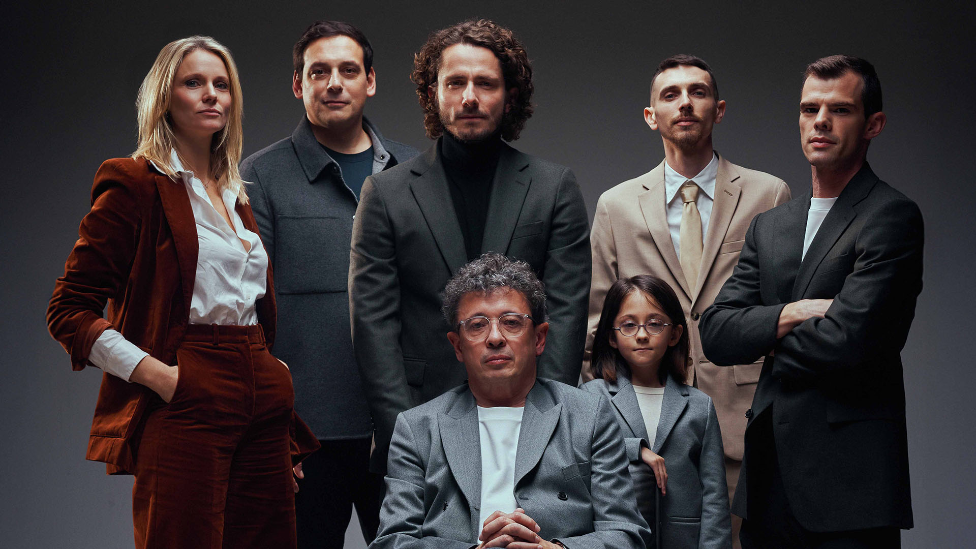Portrait de groupe illustrant le Legend Tour 2026 de Guillaume Pley : sept personnes posent dans un studio au fond sombre, dont un homme assis dans un fauteuil au premier plan et six personnes debout autour de lui.